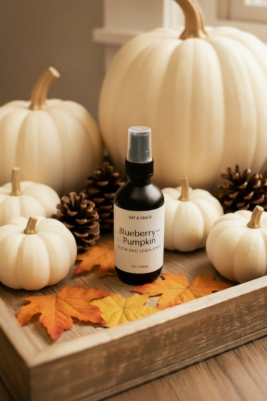Bottle of 'Blueberry & Pumpkin' room and linen spray on a wooden tray with white pumpkins, pine cones, and autumn leaves