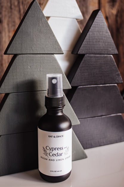 Bottle of Kat & Gracie Cypress and Cedar Room and Linen Spray against a wooden tree background.