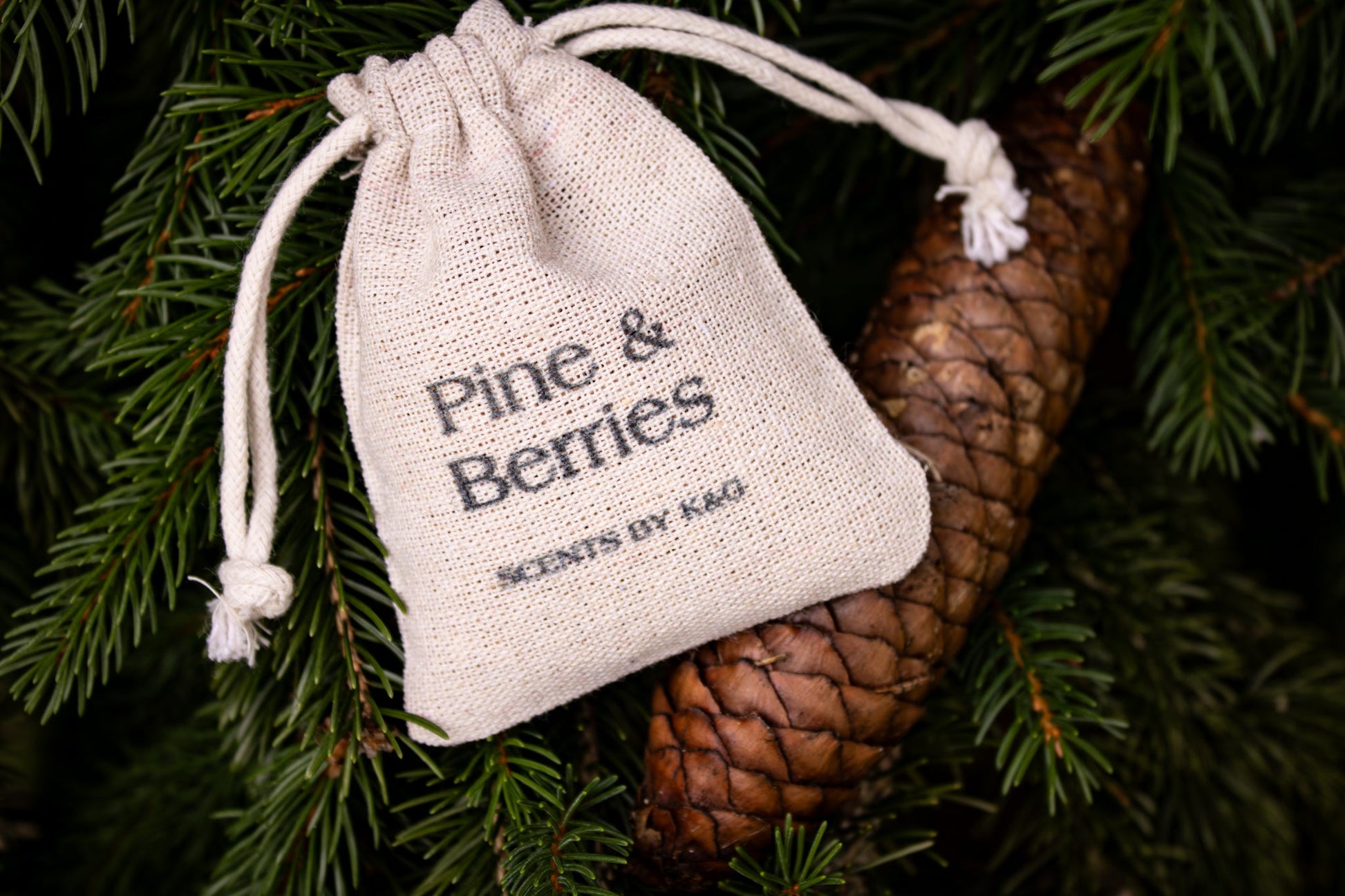 Small drawstring bag labeled 'Pine & Berries' on a pine branch with a pine cone.