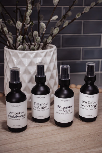 Four bottles of room sprays on a wooden surface with a vase of willow branches in the background.